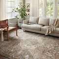 Rug styled in a bright living room under a sofa, surrounded by modern neutral furniture and large windows