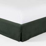 Close-up of corner bed skirt with a subtle slit in dark green linen fabric