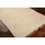 Close-up of corner on rectangular jute rug showing texture and fringed edge on dark wood floor