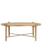 Round outdoor coffee table with natural teak wood slatted top and brass X-cross support under four tapered legs