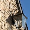 Side angle of lantern on stone wall showing curved hook detail and shadow on wall