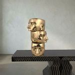 Side view of the stacked gold face sculptures displayed on a textured black table against a beige wall