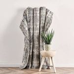 Rug draped over wooden stool next to green potted plant against a wall