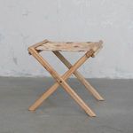 Side view of stool against textured gray wall and floor background showing natural wood and woven seat
