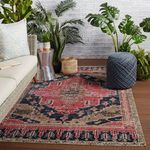 Rug styled in outdoor seating area with wicker sofa, blue pouf, and tropical plants