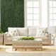 Living room scene with woven outdoor side table, sofa, and armchairs against green plant wall and white windows