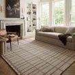 Bradley Rose / Blush Rug styled in a living room with sofa, leather chair, and large windows on wood herringbone floor