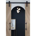 Styx Vertical Pendant in brass finish hanging in black and wood doorway with dark wall backdrop