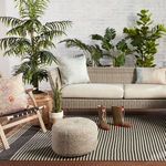 Outdoor porch view with rug under sofa, pillows, pouf, and surrounding greenery