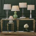 Deville Table Lamp shown on the right side on gold and glass console table in a room with dark green walls