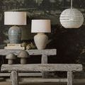 Mimi Ivory Table Lamp styled on rustic wooden bench alongside other lamps and decorative items in a dark room setting