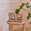 Two natural jute photo frames of different sizes styled on a round wooden stool with a green plant in background