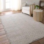 Rug styled in bright living room with light hardwood floor, armchair, and small wooden table