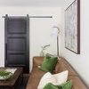 Natural sand-colored Nolita sofa with green pillows in a minimalist room featuring white walls and black door.