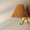Single wall sconce with aged brass arm and woven rattan shade against neutral wall