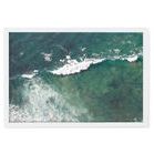 Aerial photograph of green-blue ocean waves with surfers paddling near the breaking surf