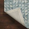 Blue-green rug corner flipped up revealing woven backing and stitched edge detail