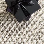 Close detail of black gift box with satin bow resting on textured chunky knit wool rug