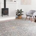 Lucia rug shown in bright room with wood-burning stove, gray chair, and potted plant