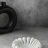 Side view of white marble ruffled bowl showing scalloped edges and textured gray surface with decorative black vase in bac...