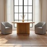 Two Sandy Rolling Dining Chairs flanking a round wooden dining table in a sunlit room with large grid window