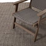 Darla rug under brown woven chair highlighting rug’s scale and indoor styling