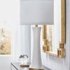 Lamp on dark console table below gold-framed mirror with soft natural lighting