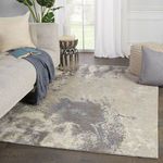 Rug styled in living room setting with beige sofa, gray throw, pouf, and natural light from window