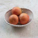 Higher angled view of the colander with three grapefruits on textured surface