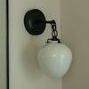 Side angle of the sconce highlighting chain-link metal arm and cord running along wall corner