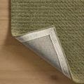 Back corner of olive rug lifted to reveal branded fabric backing on wooden floor