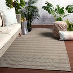 Indoor setting with gray rug on wood floor next to wicker sofa, tropical plants, and decorative pillows