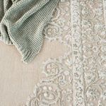 Close-up showing textured floral and scrolling border detail alongside green knitted throw on rug