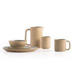 Natural speckled clay mug styled alongside matching pitcher, bowl, and plates with white background