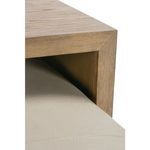 Close-up showing oak wood side table corner resting over edge of ottoman's beige leather cushion