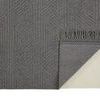 Back corner of charcoal gray rug turned to show textile backing and edge detail with fringe