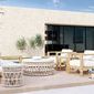 Coastal Teak Club Chair shown in outdoor patio setting paired with matching furniture and stone wall backdrop