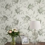 Wallpaper applied on wall behind wooden table with glass vase of flowers, books, photo frame, and pleated white lamp