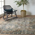 Rug in indoor setting with black rocking chair and potted plant on light hardwood flooring