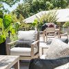 Laguna Club Chair among outdoor patio furniture, decorative pillows, plants, and railing with residential building in back...
