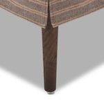 Close-up of wood leg with metal foot pad beneath striped fabric and corner details