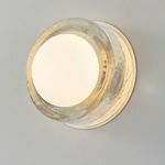 Angled view of round sconce glowing warm white with hammered aged brass finish on wall