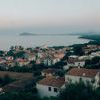 A serene coastal marina scene with red-tiled roofs on hillside and calm sea at dusk under pale sky