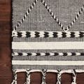 Detail of Sawyer Black Rug edge on wood floor showing tassels and striped woven border design