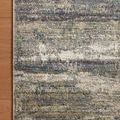 Corner detail of rug on wood floor highlighting edge binding and mixed blue, gray, and beige fibers