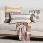 Throw blanket entwined with matching striped pillows displayed on cream sofa for coordinated living room look