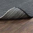 Rug edge flipped to show reverse side pattern and polypropylene weave texture on wood floor