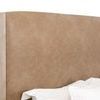Close-up of curved tan upholstered headboard with white bedding pillows partially visible