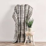 Rug draped over wooden stool beside potted plant against plain wall showing flexibility and thickness