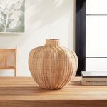 Light-toned woven vase styled on wooden table beside stacked books and natural light window